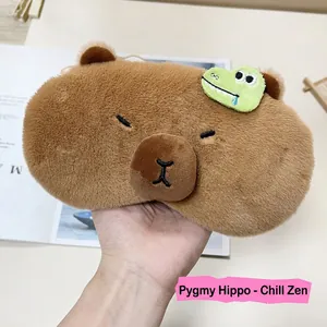 Cute Capybara plush sleep mask with green crocodile patch held over a magazine