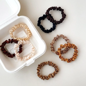 Flat lay of small silk satin hair scrunchies in neutral shades on white background