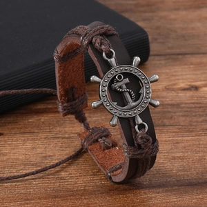 Macro shot of brown leather woven bracelet with a vintage metal rudder steering wheel charm