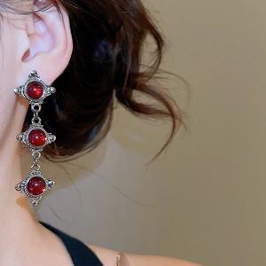 Close-up of triple-layered silver drop earrings with red resin gems on a female model