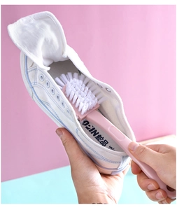 Detail view of pink long-handle cleaning brush scrubbing the inside of a white canvas shoe