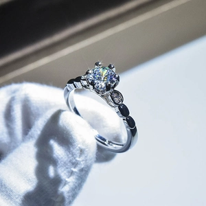 Close-up of a brilliant-cut gemstone ring held by a gloved hand with bokeh background