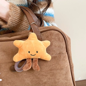 Close-up of a yellow plush star charm with a smiley face hanging on a brown suede bag