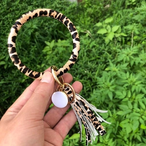 Leopard print PU leather bracelet keychain with white tassel held against green plants