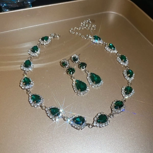 Detailed view of silver necklace and teardrop green gems on a golden jewelry tray