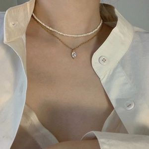 Detail of layered gold necklace with zircon pendant and white pearl choker on neck
