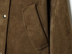 Gros plan d'une veste effet suédine avec texture marron olive et bouton en métal doré