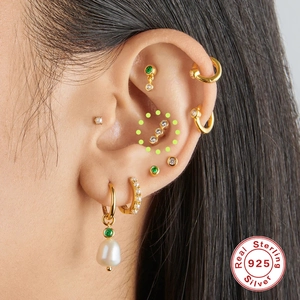 Macro shot of gold S925 sterling silver ear studs with pearls and green zircons