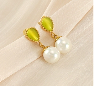 Détail de boucles d'oreilles dorées avec pierre oeil-de-chat verte et perle blanche