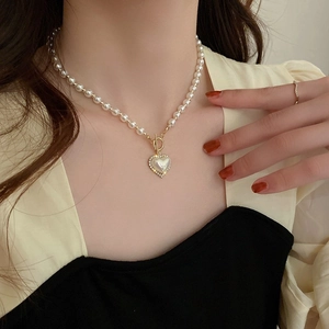 Close-up of heart pearl necklace with golden OT clasp worn by a model in warm light