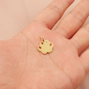 Golden paw-shaped pendant with inset crystal held in palm against a pink fabric background
