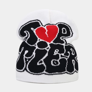 Detail of white knit beanie featuring black bubble text and a red broken heart pattern