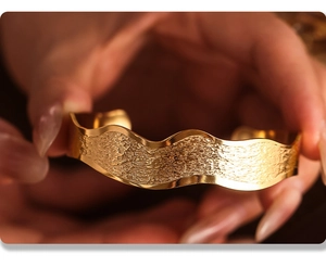 Macro detail of gold wave textured stainless steel cuff bracelet with matte hammered finish