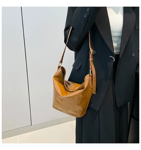 Detail of glossy caramel brown leather shoulder bag with adjustable gold metal buckle