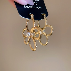 Macro detail of gold flower earrings with central pearl on a black display card