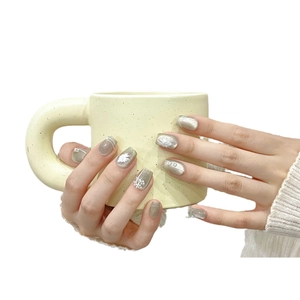 Handmade silver cat-eye press-on nails with white floral art and pearls on a ceramic cup