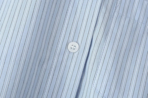 Detail of light blue striped cotton fabric with white button and precise stitching