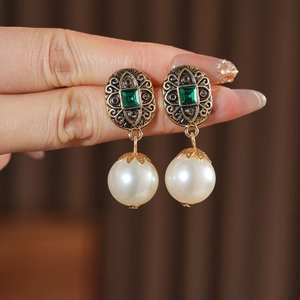 Dettaglio di orecchini vintage in ottone con gemme verde smeraldo e grandi perle d'imitazione