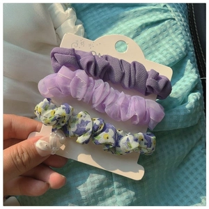 Three-piece set of floral and mesh fabric scrunchies in purple shades held on a card