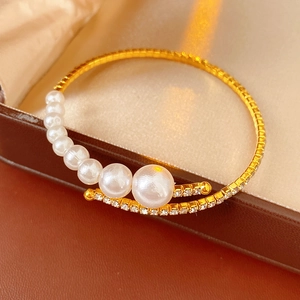 Detailed close-up of a gold-plated open wire bracelet with crystals and pearls