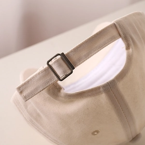 Close-up of cream baseball cap back with adjustable metal buckle and twill fabric detail