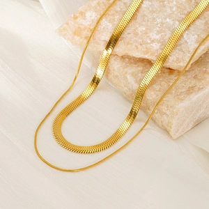 Detailed view of layered gold snake bone chains resting on natural marble and white silk