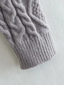 Dettaglio del maglione grigio a maglia con trama a treccia e polsini a coste rifiniti