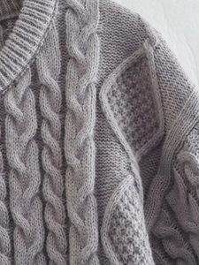 Dettaglio ravvicinato di un maglione grigio a trecce con trame a rombi in evidenza