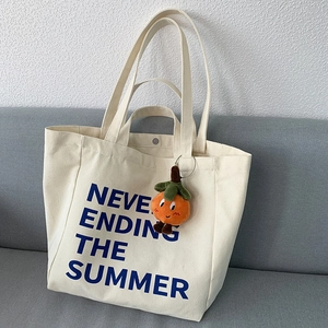 Detail of a beige canvas tote bag with a plush orange persimmon charm and blue text