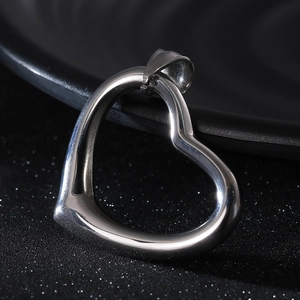 Macro view of a polished silver hollow heart pendant on a textured black surface