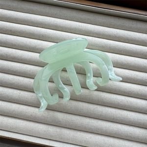 Detailed view of translucent mint green resin octopus hair claw on soft grey velvet tray