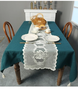 Detail of dark green tablecloth with fringe and cream white floral lace table runner