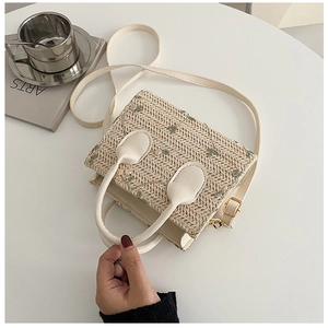 Detail of square straw woven handbag with green flower embroidery and white leather strap