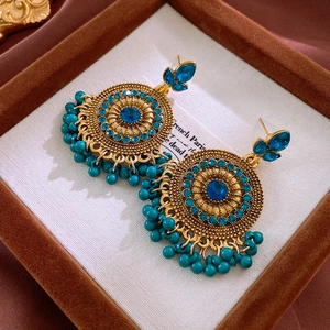Gros plan de boucles d'oreilles vintage dorées avec cristaux bleus et pompons en perles