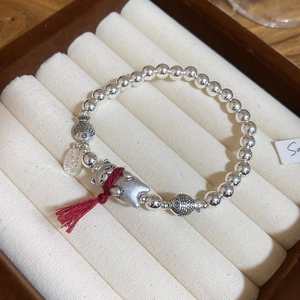 Dettaglio del bracciale con perline d'argento, ciondolo Maneki Neko e nappe rosse