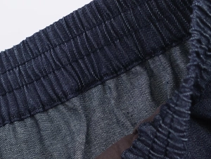 Detail view of elastic waistband on dark blue denim trousers with twill fabric texture