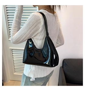 Close-up of a glossy black patent leather hobo bag with embossed logo worn by a model