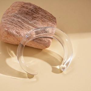 Macro shot of a transparent acrylic open bangle on a natural stone base with soft warm lighting