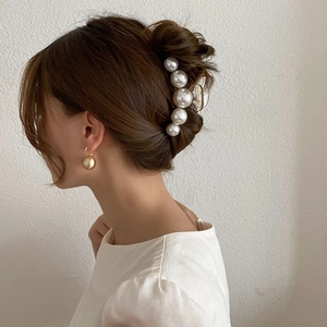 Detailed view of elegant hair claw clip with white pearls and gold metallic earrings