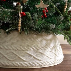 Detail of white cable knit Christmas tree skirt with festive holiday decor on wooden floor