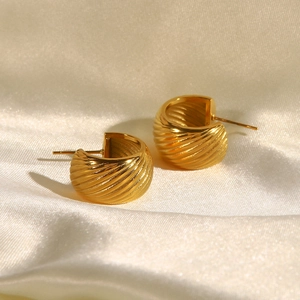 Macro shot of gold-finished C-shaped textured earrings on elegant beige silk fabric