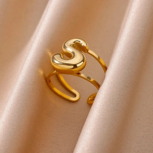 Close-up of golden letter S open ring nestled in elegant beige satin fabric folds