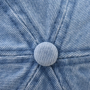 Detail of light blue denim baseball cap showing top button and reinforced stitching