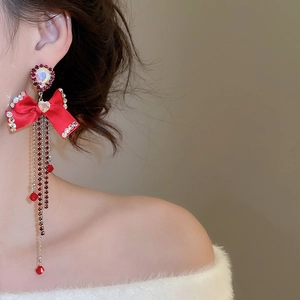 Close-up of red ribbon bow earrings with cascading tassel chains and sparkling rhinestones