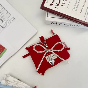 Close-up of red fabric coin purse with pearl bow and heart pendant on white desk