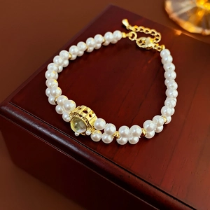 Detail of gold plated pearl bracelet featuring moonstone fish tail charm on a red jewelry box
