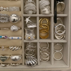 Collection of silver and gold rings with gemstones in a beige jewelry storage box
