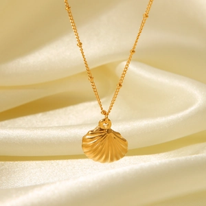 Macro shot of gold shell pendant on thin bead chain resting on beige silk fabric