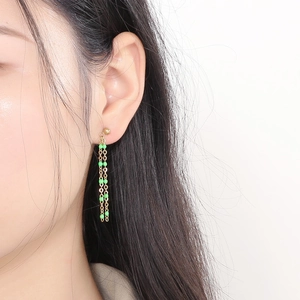 Close-up of minimalist gold tassel earrings with green beads worn on ear model