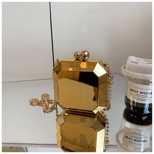 Detailed view of the gold geometric acrylic box clutch with metal chain on a mirror surface